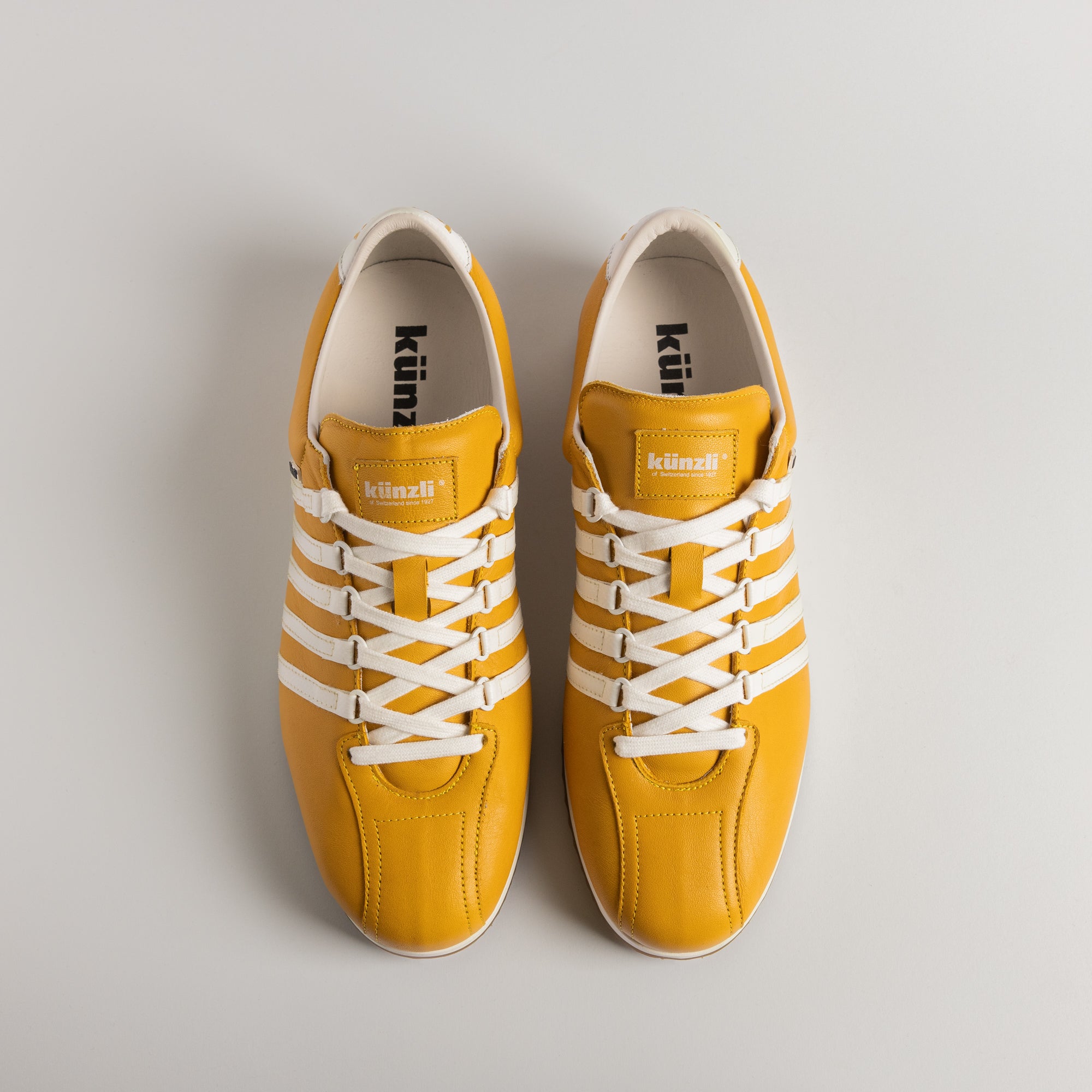 Ein gelber und weißer Kuenzli Sneaker auf hellem Hintergrund.