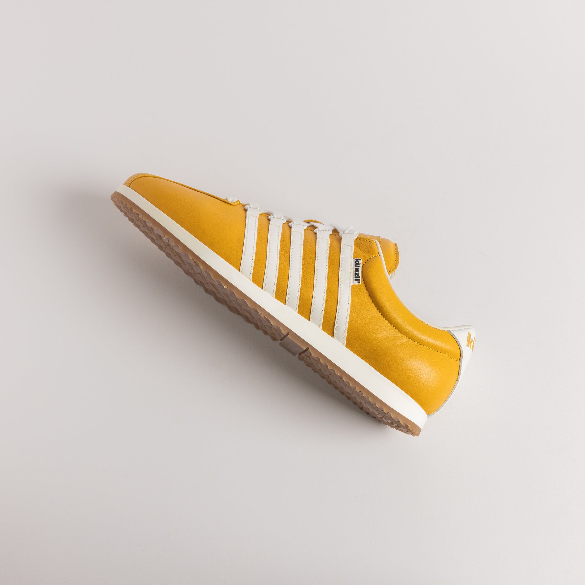Ein gelber und weißer Kuenzli Sneaker auf hellem Hintergrund.