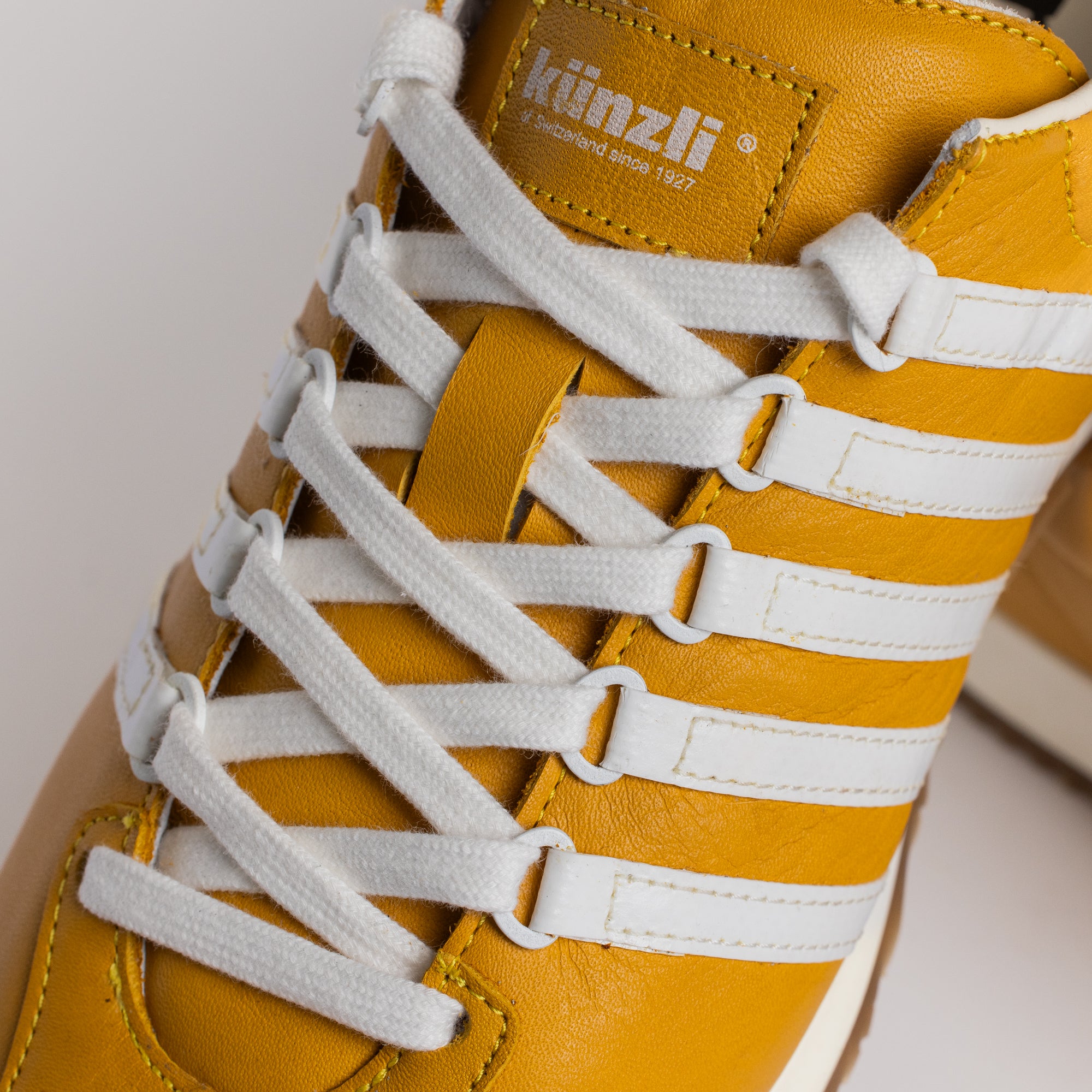 Ein gelber und weißer Kuenzli Sneaker auf hellem Hintergrund.