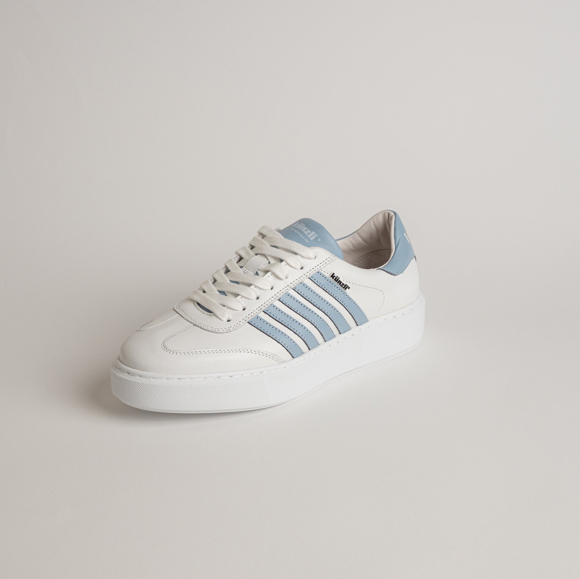 Weißer Sneaker von Kuenzli Schuhe mit blauen Streifen auf hellem Hintergrund.
