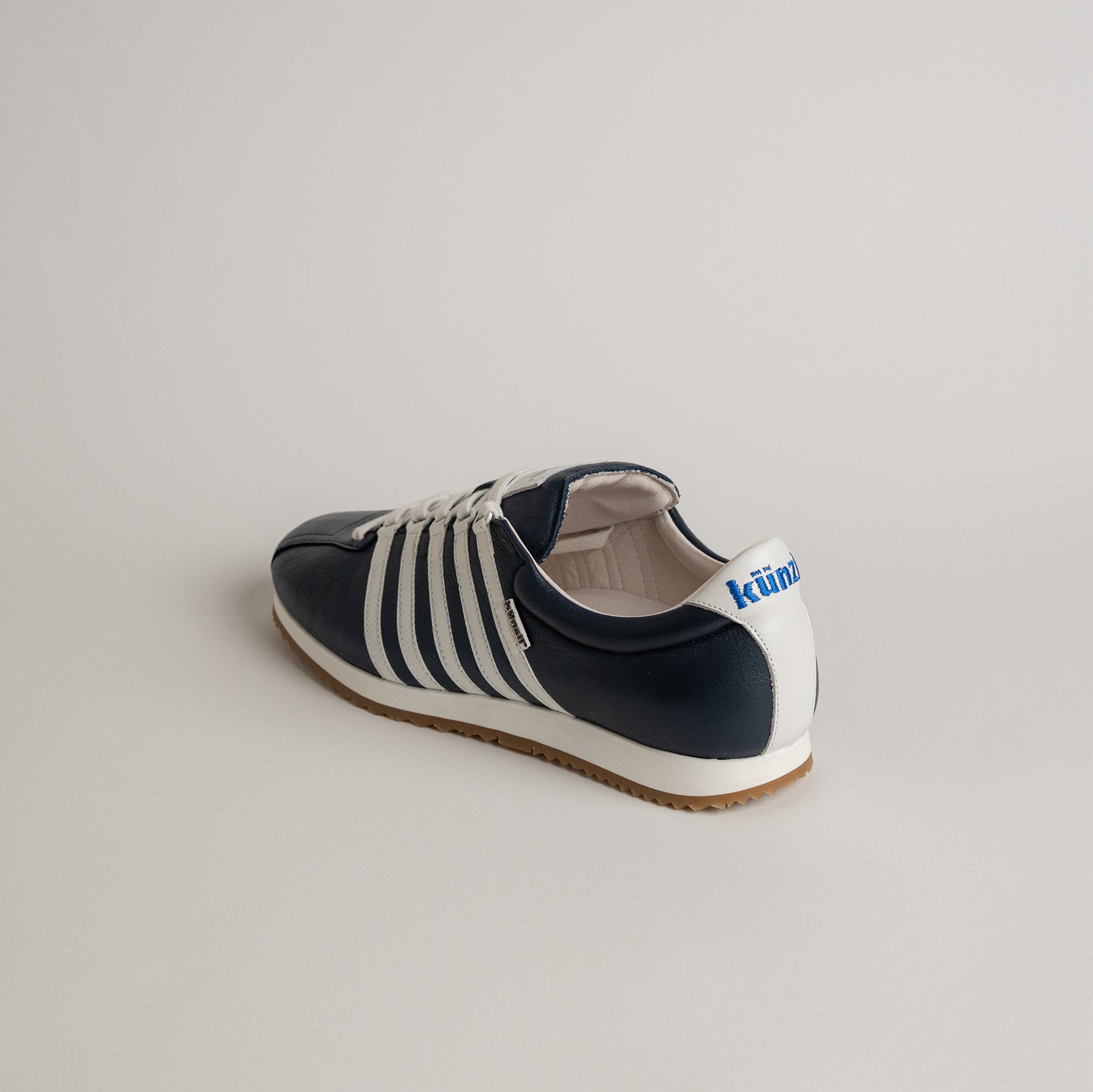 Ein dunkelblauer Kuenzli Schuh mit weißen Streifen auf hellem Hintergrund.