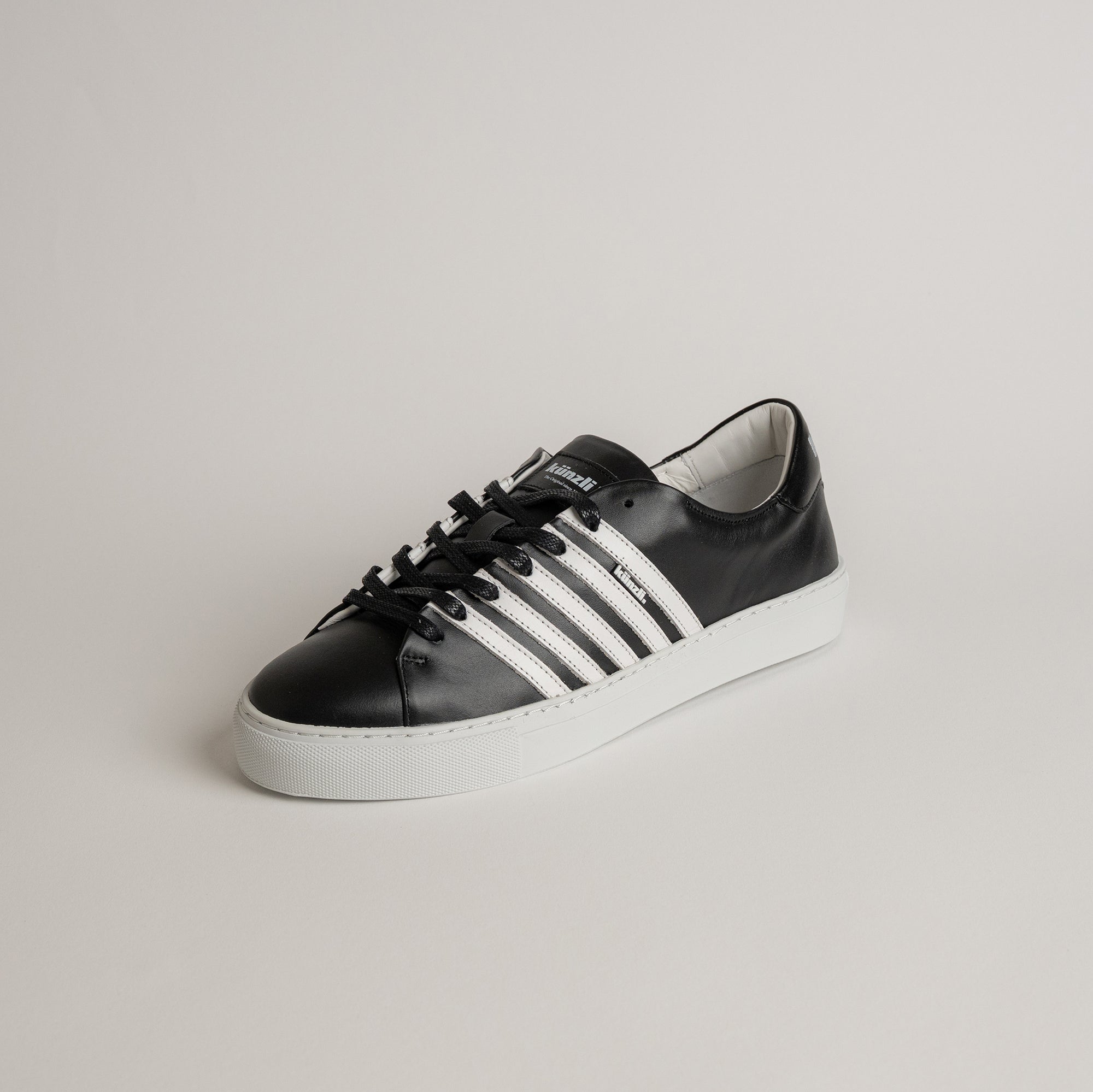 Schwarzer Lederschuh von Kuenzli Schuhe mit weißen Streifen auf hellem Hintergrund.