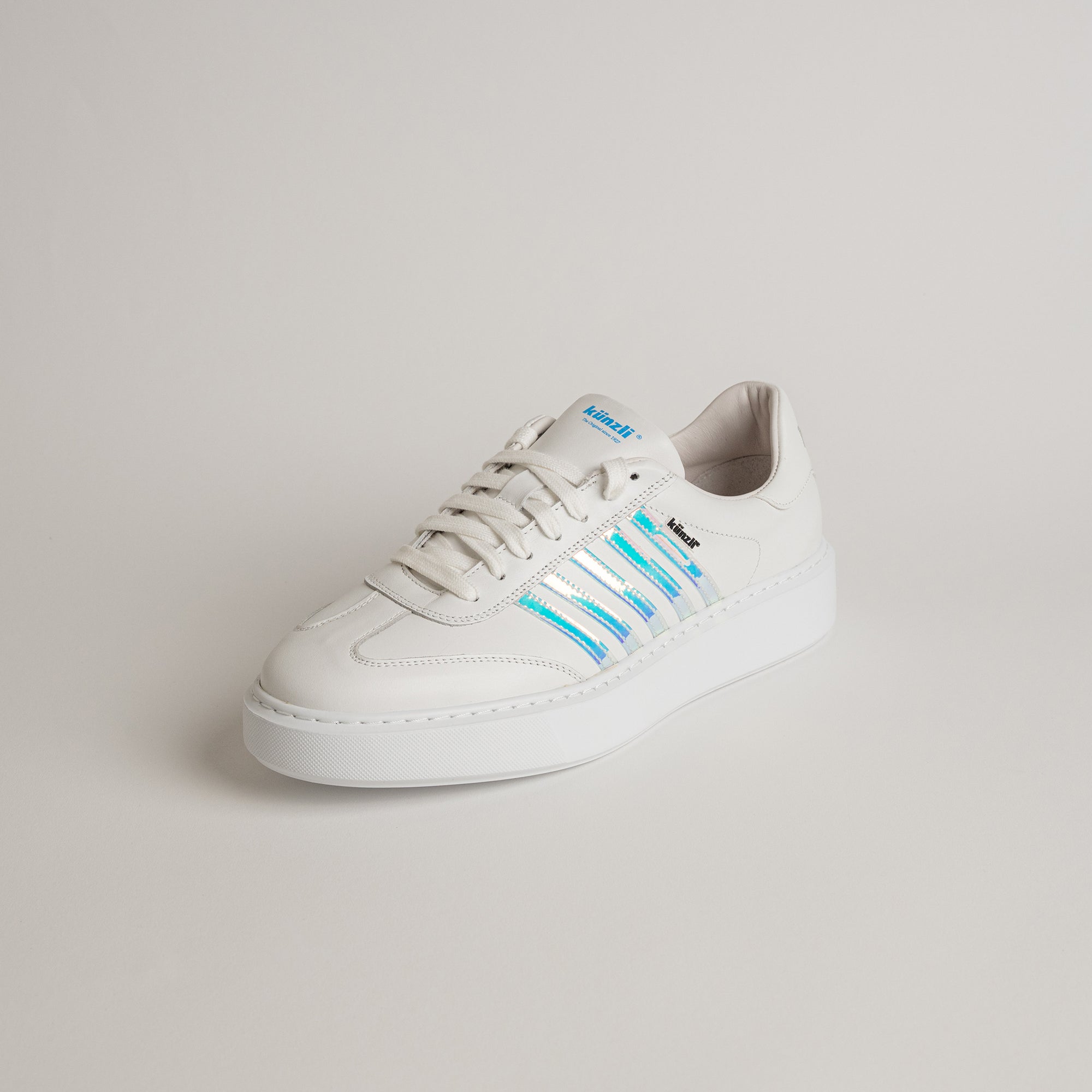 Weißer Sneaker von Kuenzli Schuhe mit blauen Streifen auf hellem Hintergrund.