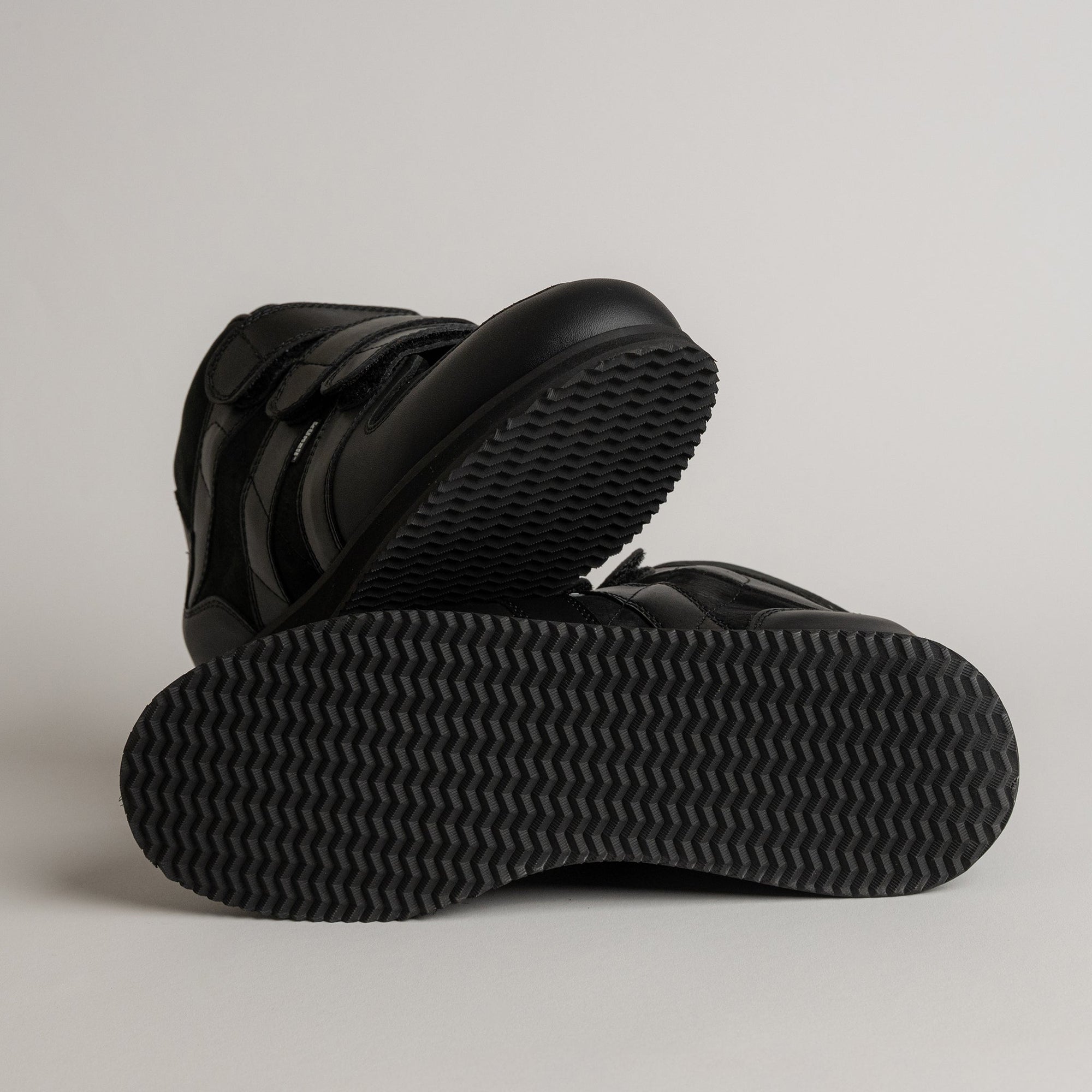 Schwarze Kuenzli Schuhe mit rutschfester Sohle auf grauem Hintergrund.