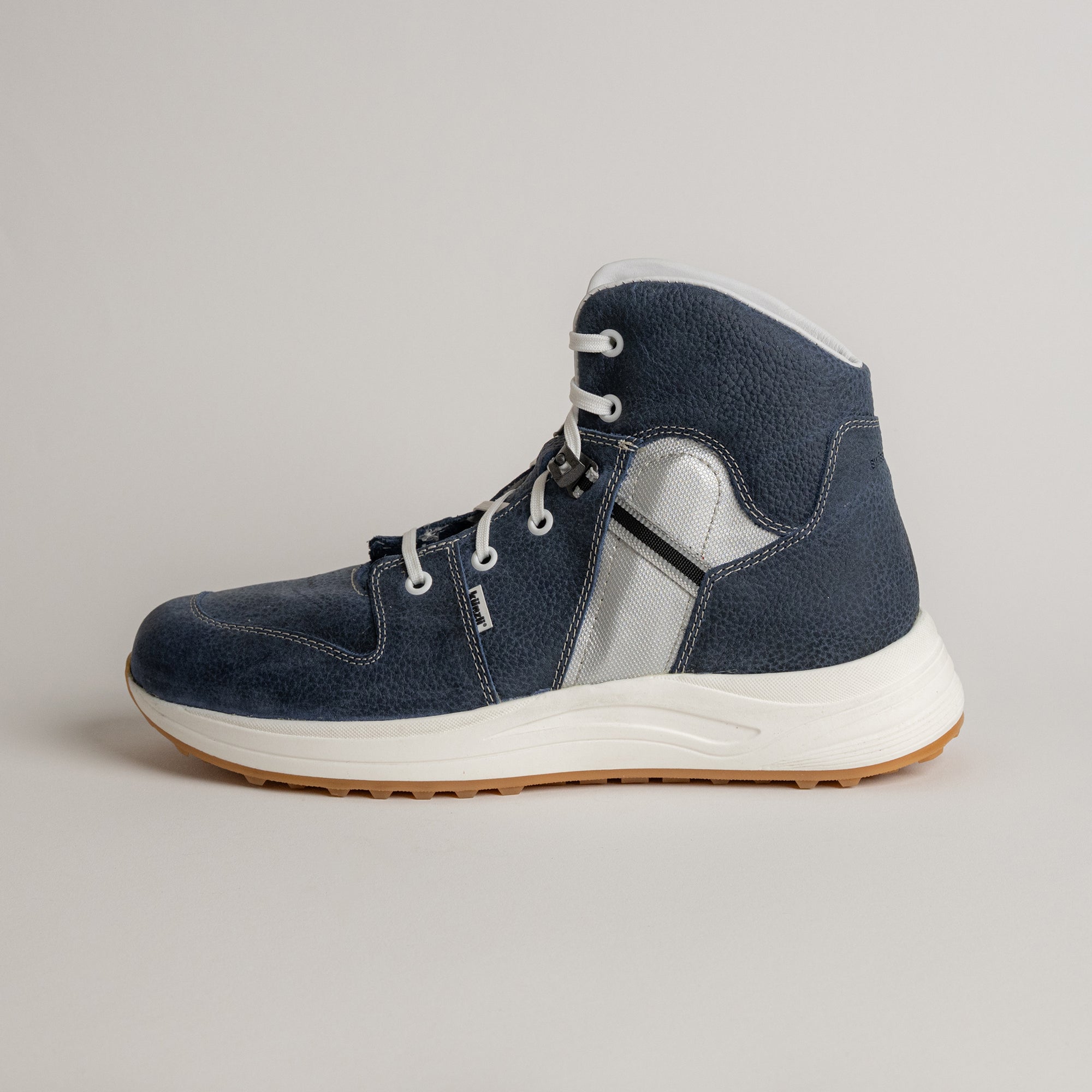 Ein blauer Kuenzli Schuh aus Leder mit weißer Sohle auf grauem Hintergrund.
