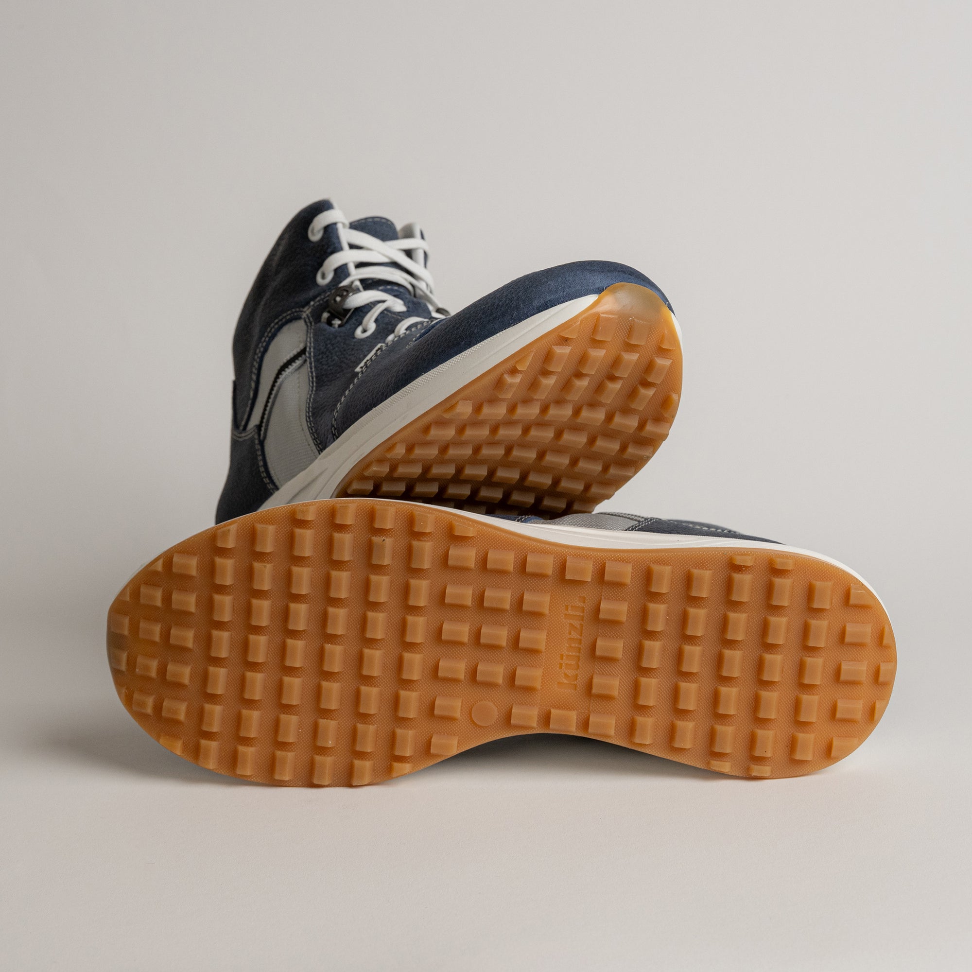 Ein Paar blaue Kuenzli Schuhe mit rutschfester, orangefarbener Sohle auf hellem Hintergrund.