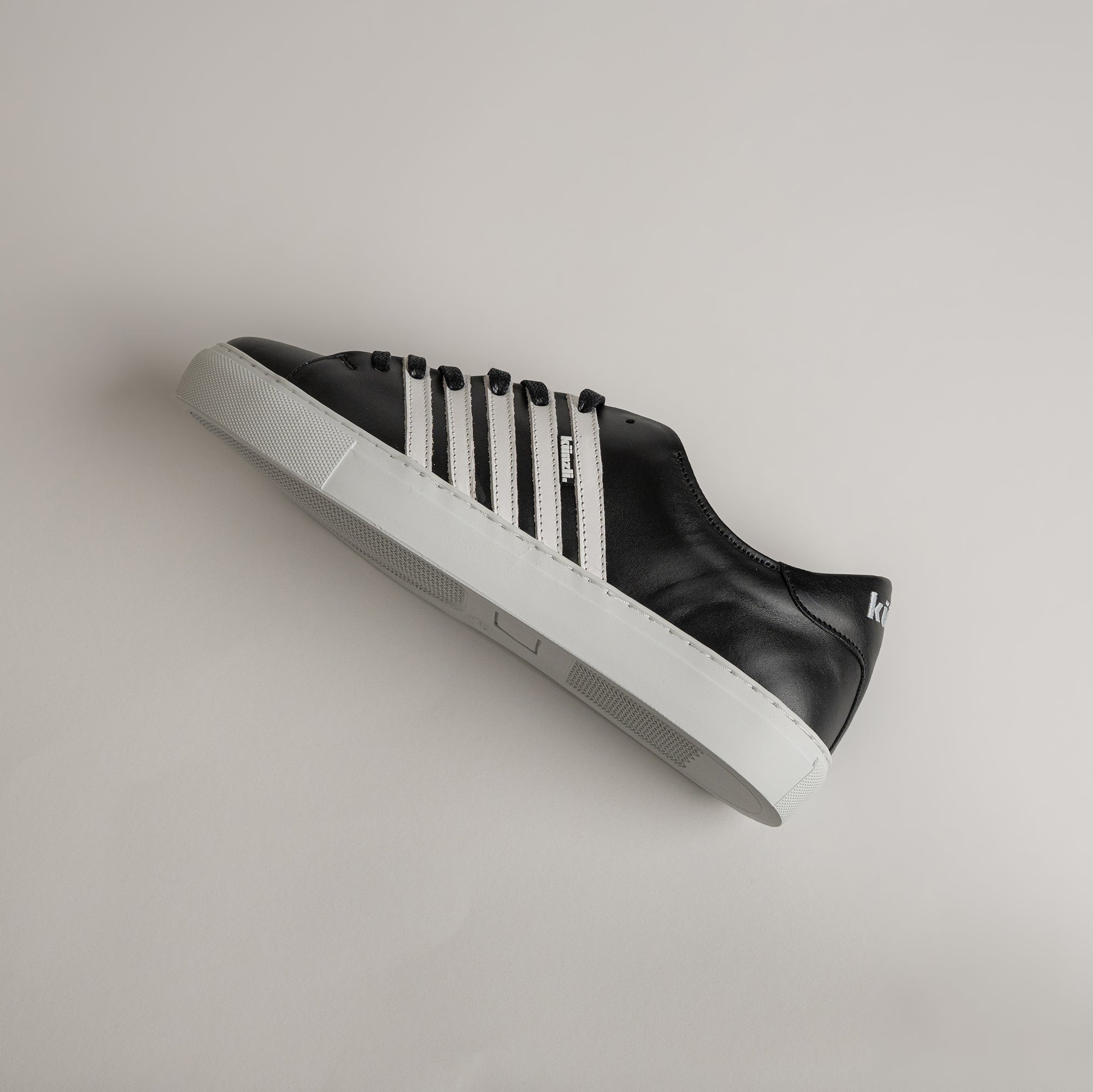 Schwarzer Kuenzli Schuh mit weißen Streifen auf hellem Hintergrund, seitlich liegend.