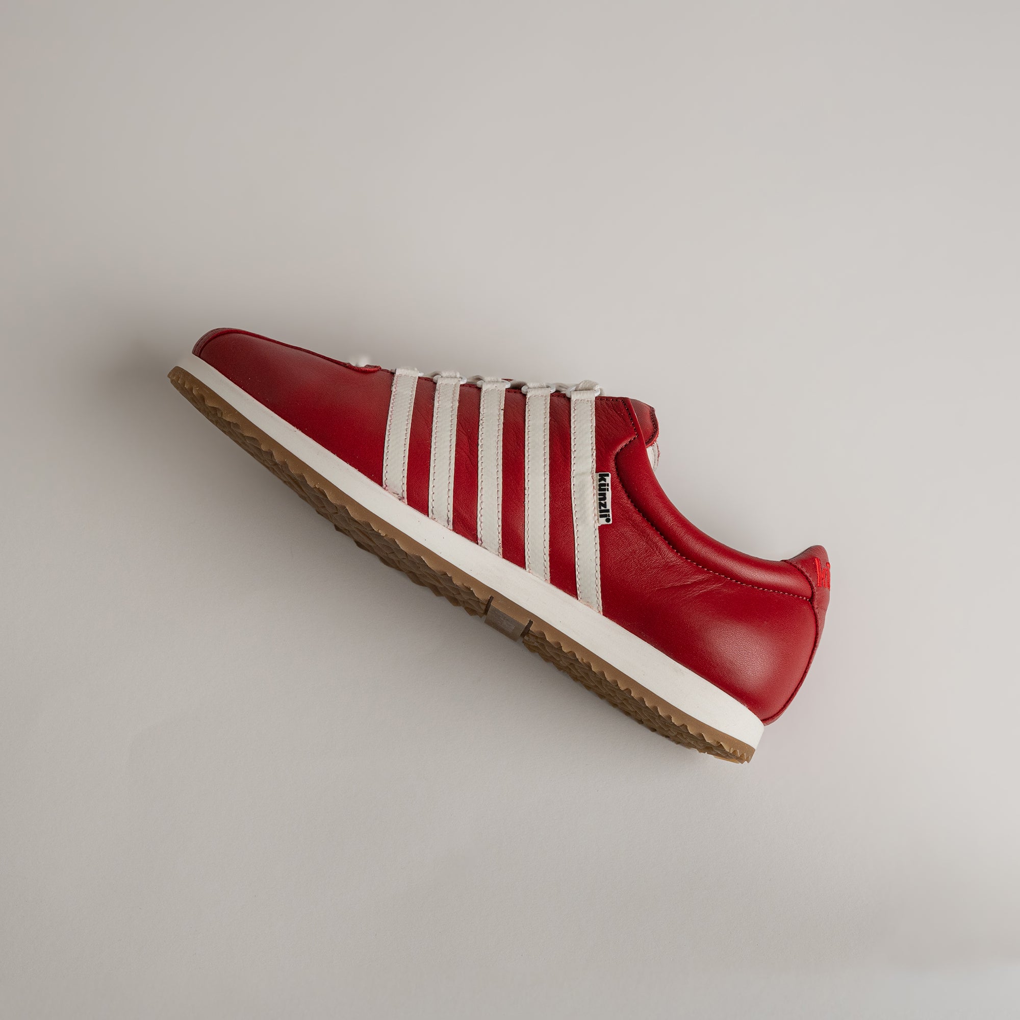 Roter Kuenzli Schuh aus Leder mit weißen Streifen auf hellem Hintergrund.