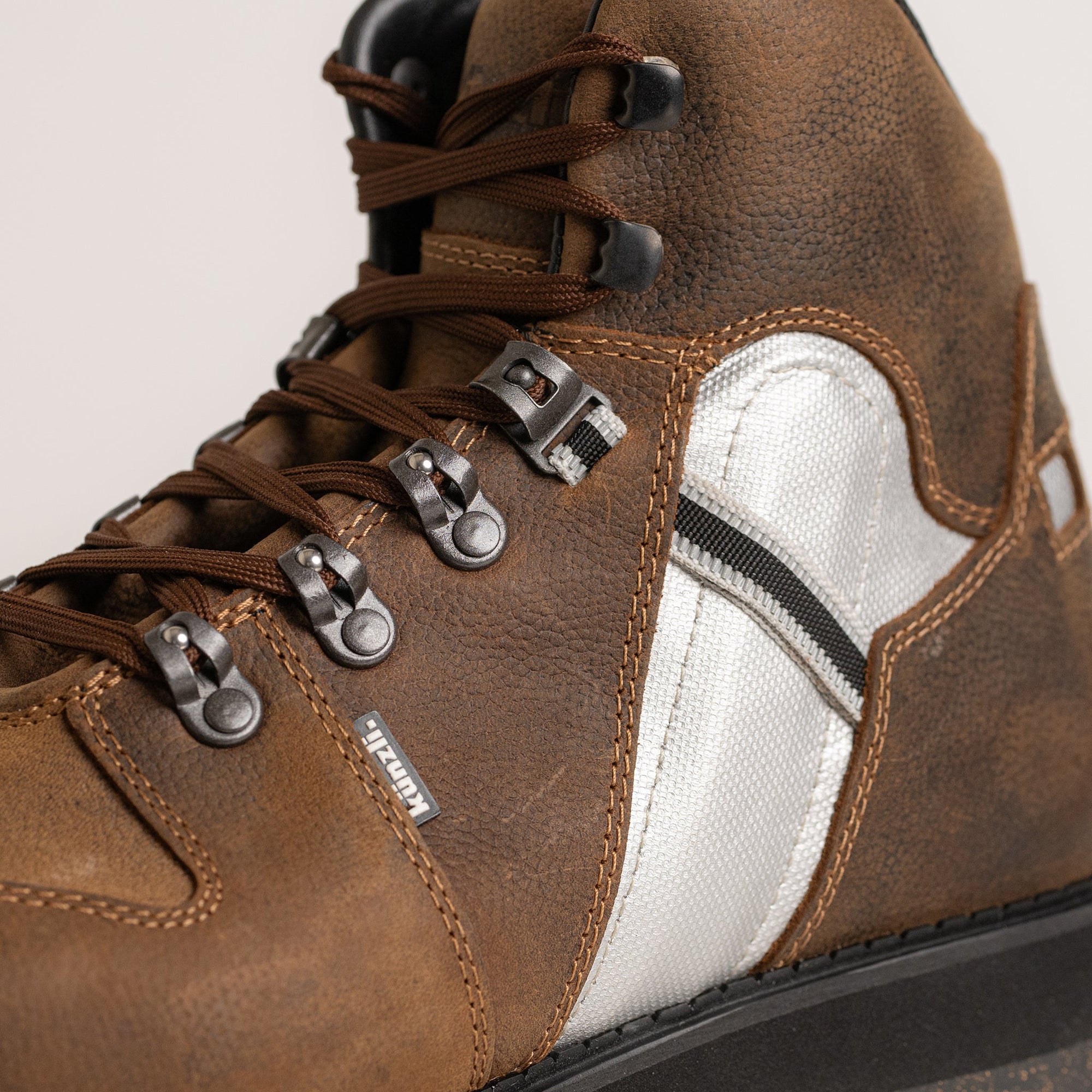 Ein brauner Lederstiefel von Kuenzli Schuhe mit robusten Schnürsenkeln und Metallschlaufen.