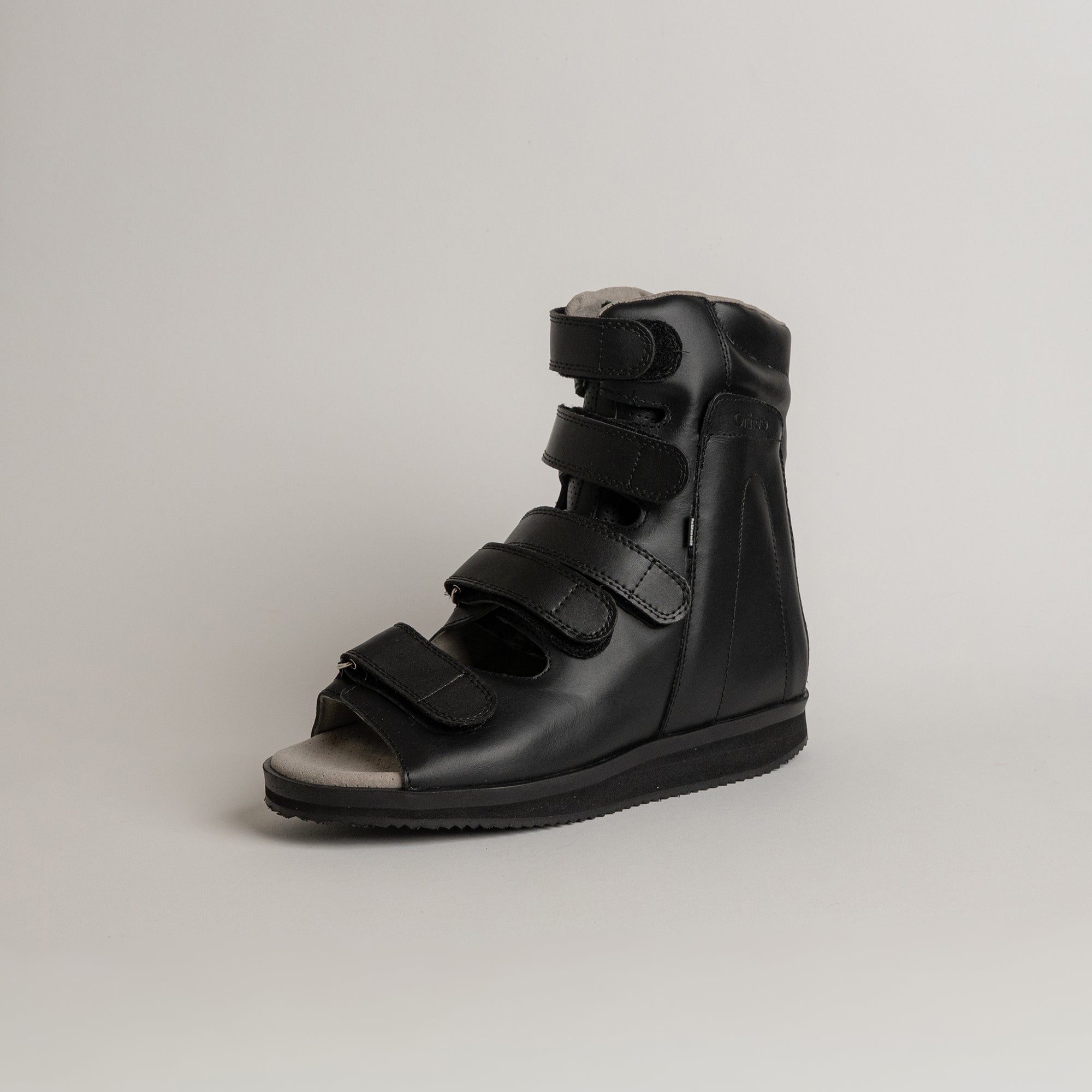 Schwarzer orthopädischer Schuh von Kuenzli Schuhe mit Klettverschlüssen auf grauem Hintergrund.