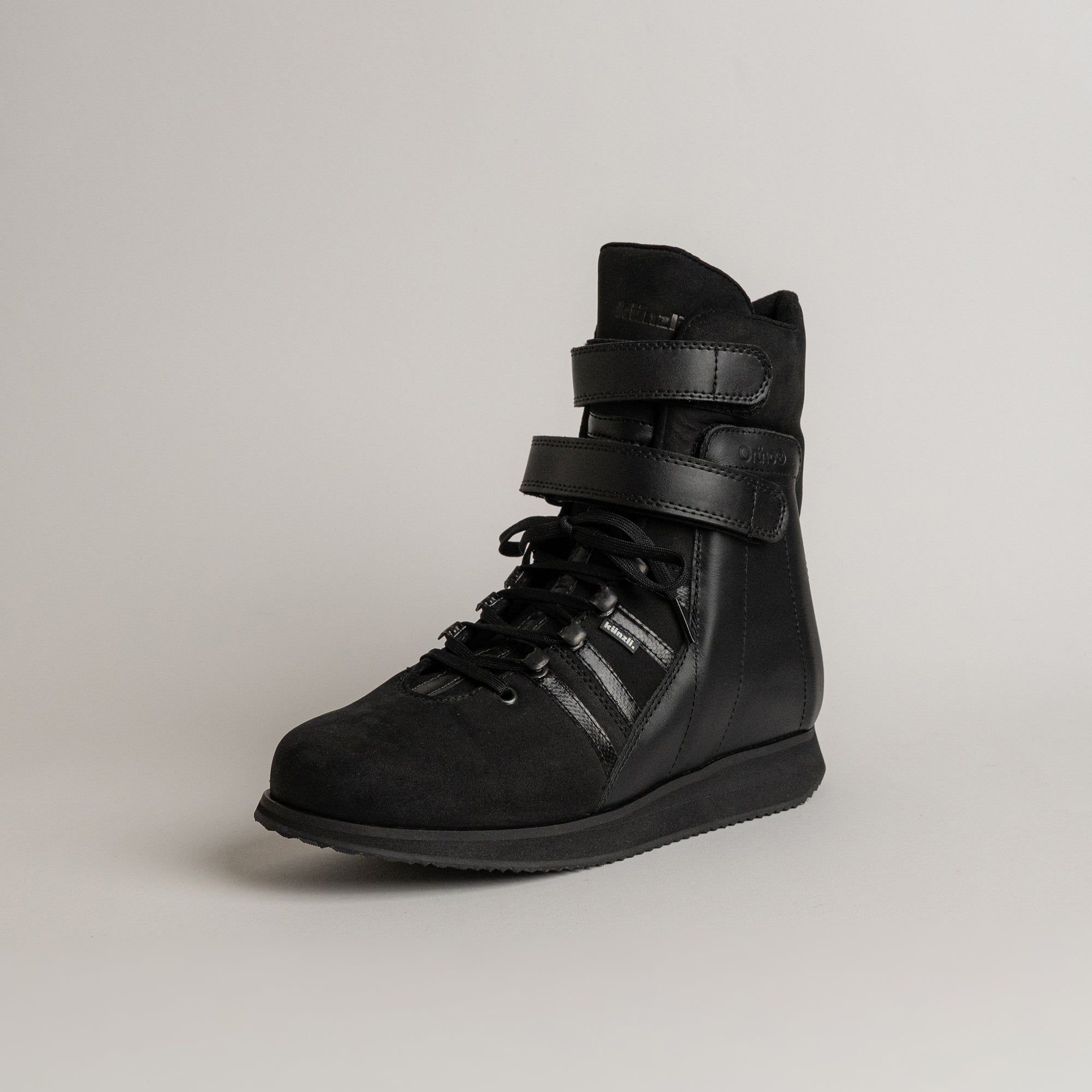Schwarzer Kuenzli Schuh aus Leder mit Schnürung und Klettverschluss auf grauem Hintergrund.
