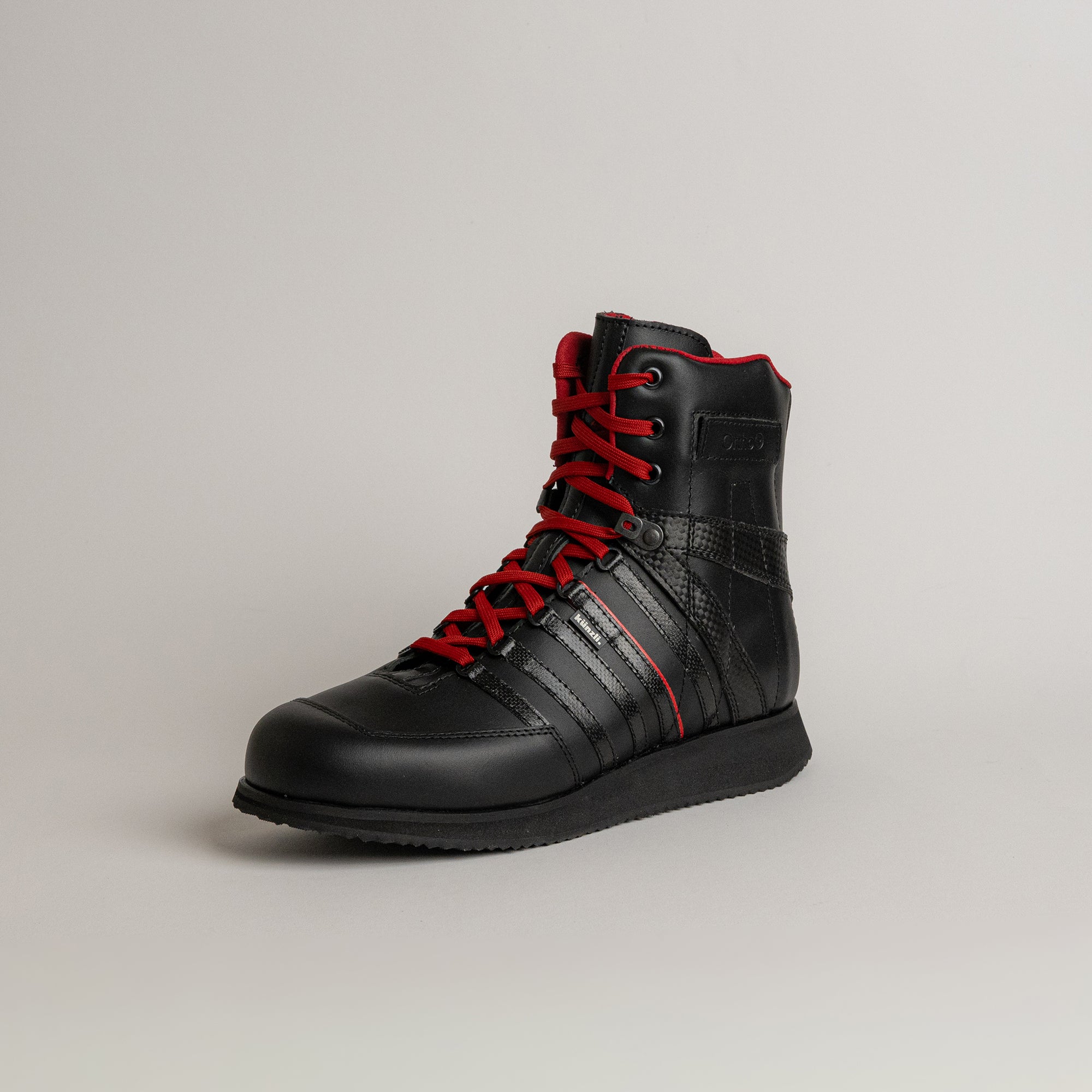 Schwarzer Lederstiefel mit roten Schnürsenkeln von Kuenzli Schuhe auf grauem Hintergrund.
