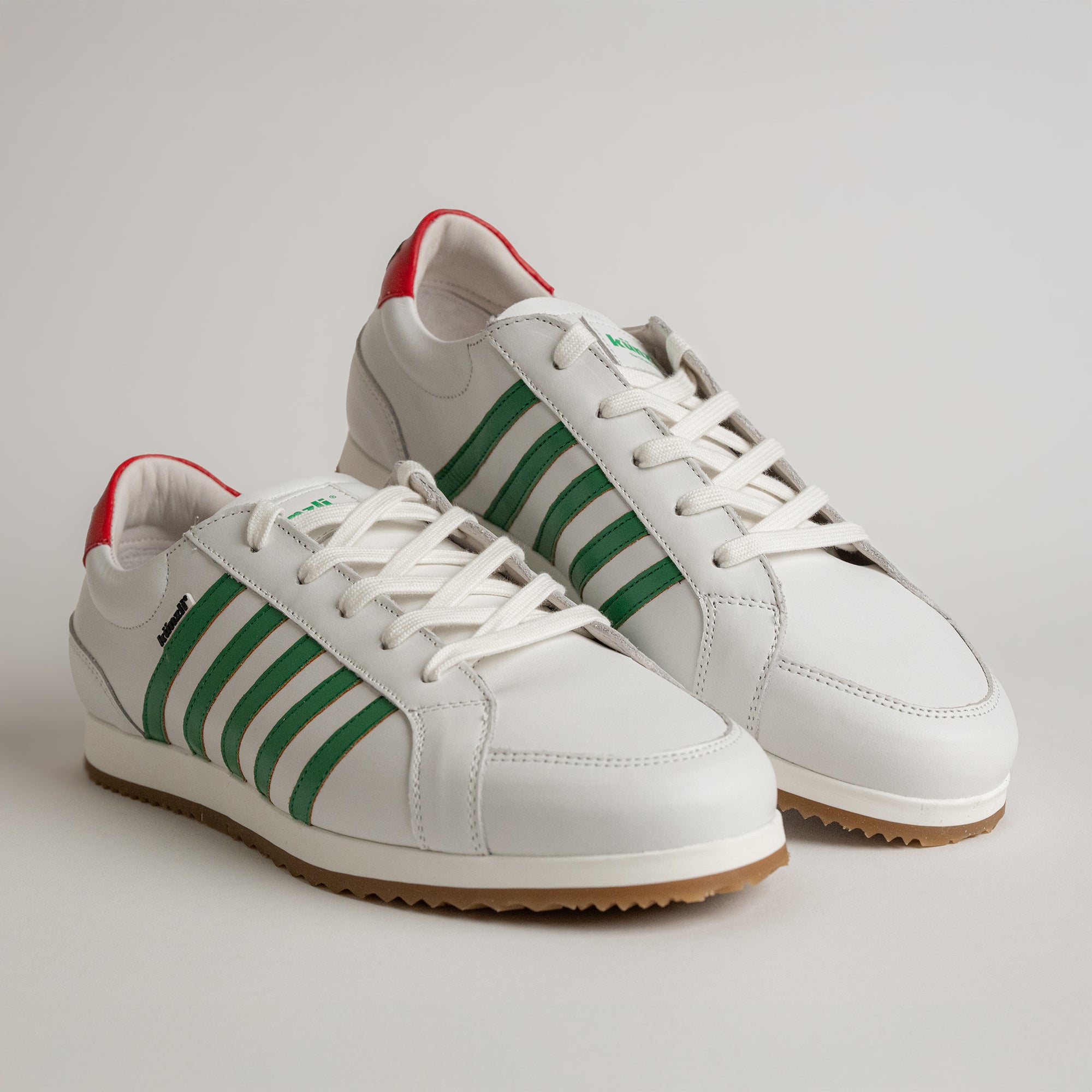 Weiße Kuenzli Schuhe mit grünen Streifen und rotem Detail auf hellem Hintergrund.
