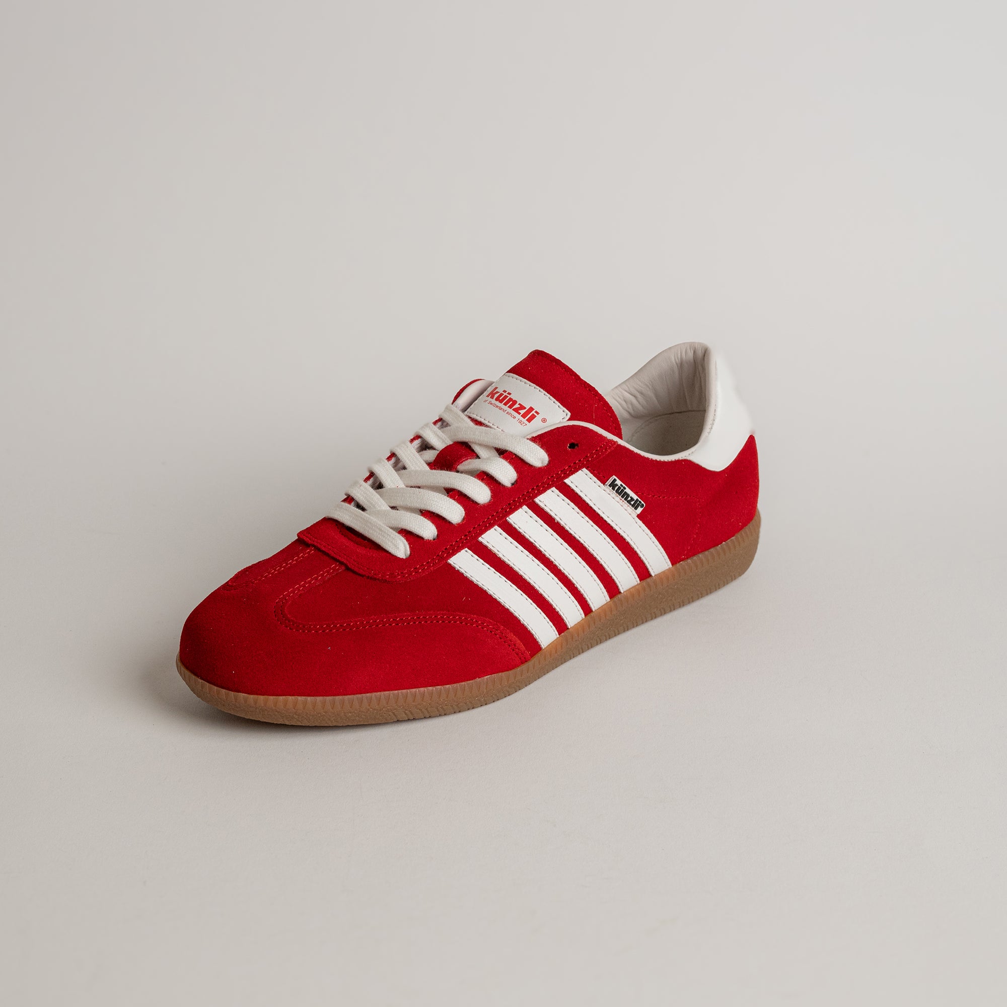 Roter Kuenzli Schuh mit weißen Streifen und Gummisohle auf hellem Hintergrund.